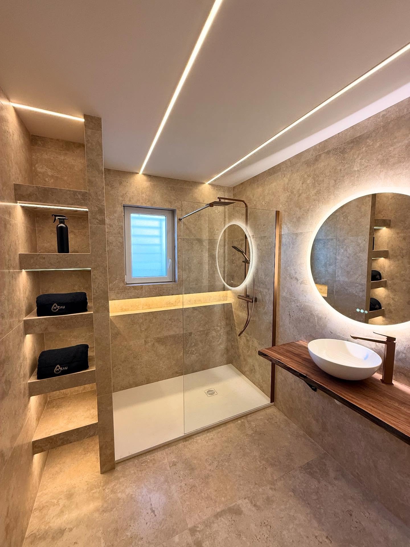 Salle de bain rénovée avec carrelage beige, grande douche et éclairage LED